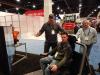 Excavator simulator was a big hit at the Helac booth. (L-R): Mark Lunstead, Helac national sales manager, had MN Roadways’ Brian Buesgens give it a shot with his co-worker, Mark Miller looking on