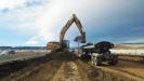 A large Cat excavator lifts dirt for a section of new highway. K-rail separates motorists from the work zone.