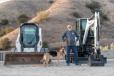 Facilities Manager Jim Wiggins and one of the canine participants take a break with a Bobcat CTL and excavator. 