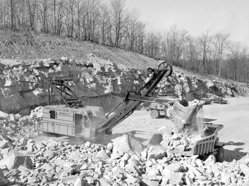 A Campanella & Cardi P&H 1055 shovel loads blasted rock into a Mack LYSW end dump truck on the big I-95 project in Groton. A Mack LVX end dump is waiting to be loaded. The photo was taken on March 29, 1963. The contractors owned 16 of the Mack LVX trucks. The first group of Mack M- 30X trucks purchased began to appear on this job.
(CTDOT photo)
