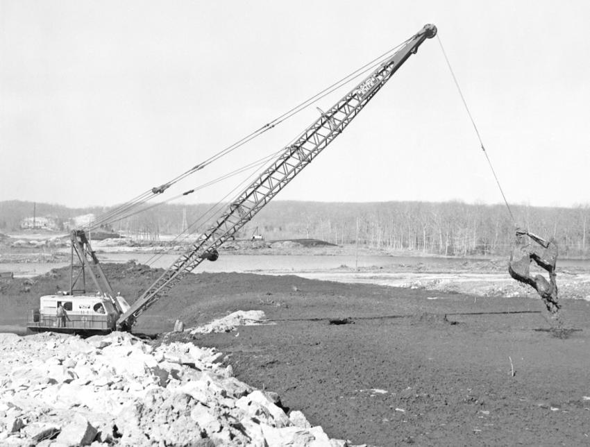 A Bucyrus-Erie 88-B equipped with a clamshell bucket is casting peat ahead of the broken rock fill on March 29, 1963. Campanella & Cardi may well have pioneered this practice. A dragline bucket, commonly used to excavate peat, unloads at or near the plumb point with the boom tip sheaves. Casting with a clamshell bucket increased your working range by an additional 20 to 30 ft. or more-eliminating a considerable amount of re-handling.
(Lanny Gray photo)