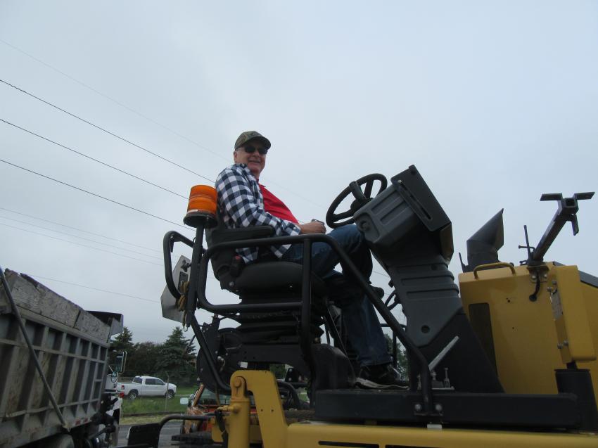 Mike Rueve of Rueve Farms, watches the auction from atop this Cat AP1055E asphalt paver while waiting to bid on a track hoe.
