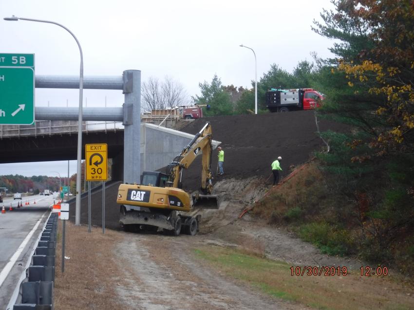 Crews install guardrail and plant grass behind a barrier on Route 102.