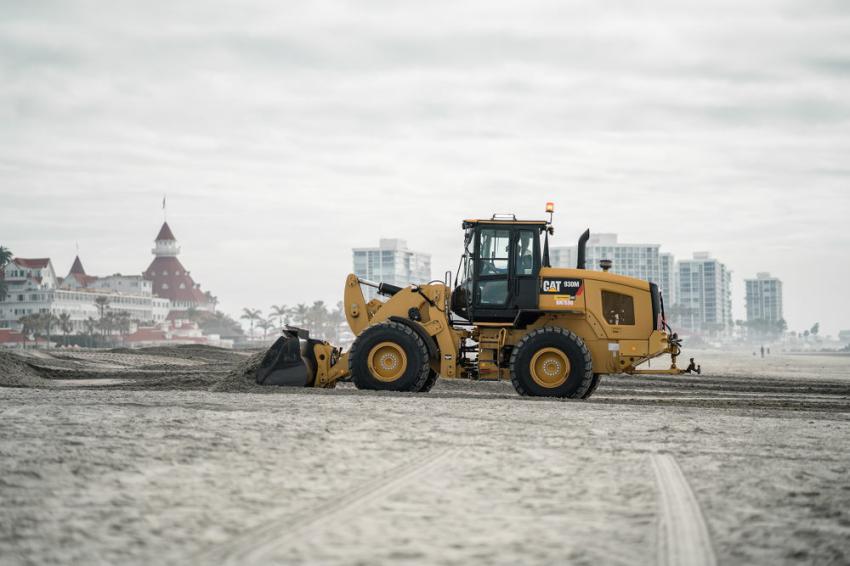 A loader cleans up the beach in Coronado with the Hotel Del Coronado visible in the background.
