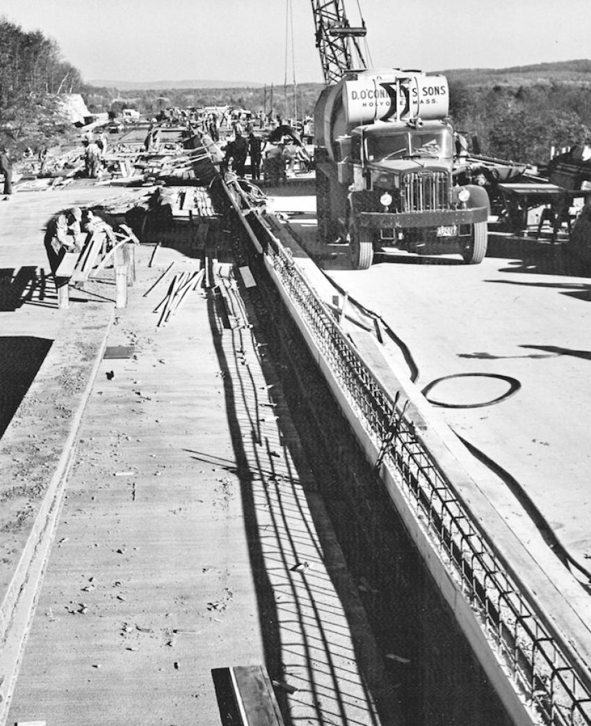 In Massachusetts — D. O’Connell’s contract for the Westfield River bridge was $2,714,414. The bridge deck is being poured in this scene. The contractor set up a batch plant near the site to supply the 12,000 cu. yds. of concrete needed. One of the firm’s Autocars with a Worthington mixer is on the bridge.
(Edgar A. Browning photo  Daniel O’Connell’s Sons Collection)