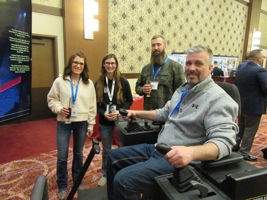 (L-R): Kelly Kominek of Stoneco of Michigan; Danielle Athey of Operating Engineers Local 324; and David Stranyak of Stoneco of Michigan watch as Kelly’s husband, Larry Kominek of Stoneco of Michigan, tries his hand at a simulator during the event.
