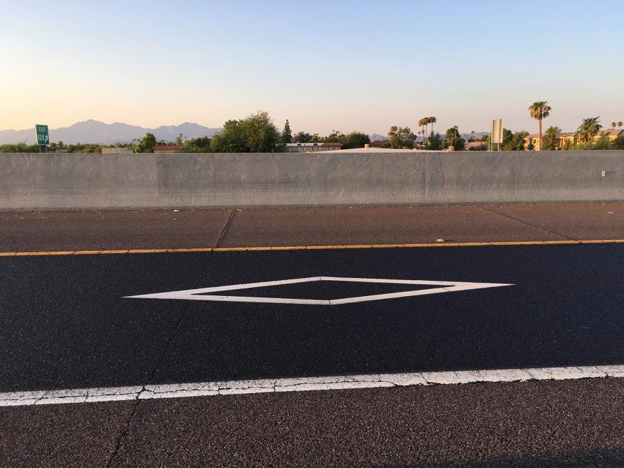 Using scrap metal, ADOT maintenance workers fashioned what’s essentially a reverse stencil — a diamond-shaped template that keeps the oil-based seal off of white HOV markings within lanes.