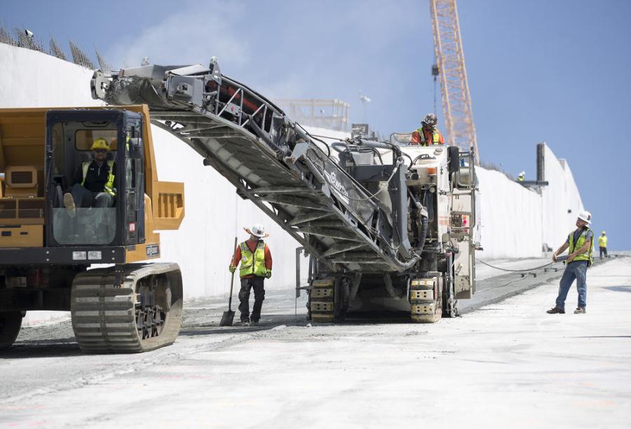 On steep spillway slope, with forward speed of 9 ft. per minute, a Wirtgen W 2100 cold milling machine prepares surface for reinforced concrete slab; millings placed in 7 cu. yd. haul vehicles, usually used in difficult open-cast mine applications.
(California Department of Water Resources photo)