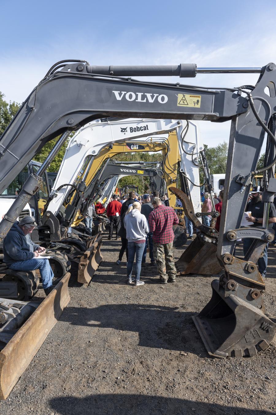 Auction attendees gather as the Sales Auction Company truck moves along the expansive selection of excavators.
