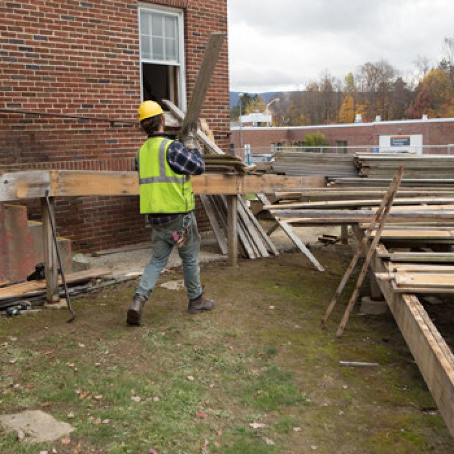 A member of the Deconstruction Works crew carries lumber to stack for reuse outside the Lodge building on the Southwestern Vermont Medical Center campus in Bennington.
