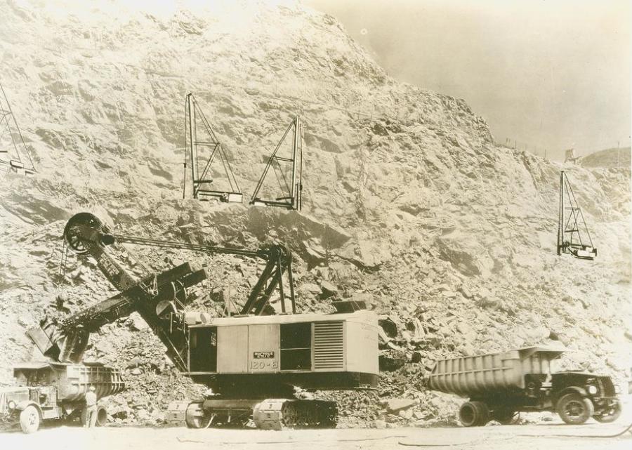 A Bucyrus-Erie 120B electric shovel loads a Mack Super Duty AP truck during construction of San Gabriel Dam north of Azusa, Calif., circa 1933. Another Mack awaits as churn drills, so named for drilling holes by an action like that of a butter churn, prepare blast holes on the bench above.
(Bucyrus-Erie Company photo/HCEA)